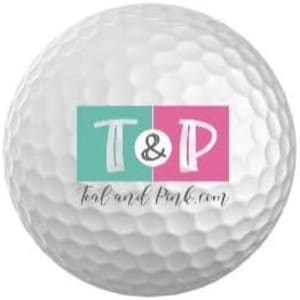 Puede incluir: Bola de golf blanca con un logotipo turquesa y rosa que dice "T&P" y "teal and pink.com"