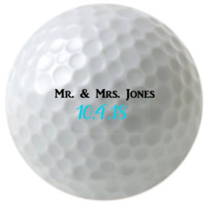 Puede incluir: Bola de golf blanca con texto negro que dice "Mr. & Mrs. Jones 10.4.18"