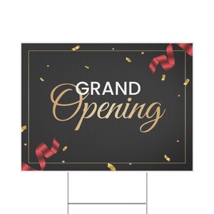 May include: A black and gold sign with the text "GRAND OPENING" in gold lettering. The sign is decorated with red and gold confetti and ribbons.