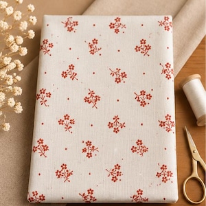 Peut inclure: Un morceau de tissu rectangulaire blanc cassé orné d'un motif répétitif de petites fleurs rouges et de minuscules points rouges. Le textile présente une texture tissée visible et est présenté comme une pièce de tissu pliée à plat.