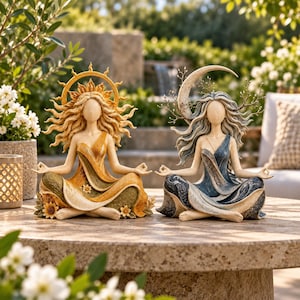 Op de afbeelding: Twee decoratieve beeldjes in een zittende meditatiehouding. Het linkerfiguur heeft een gouden zon-halo, geel en groen gewaad en zonnebloemen. Het rechterfiguur heeft een zilveren maansikkel, blauw en grijs gewaad en kale takken.