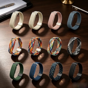 May include: A collection of twelve braided watch bands arranged in three rows. The bands feature various solid colors including beige, pink, blue, green, and black, alongside multi-colored woven patterns. Each band includes a metallic buckle.