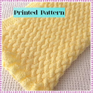May include: A close-up of a soft, yellow knitted blanket with a woven pattern. The blanket has a textured surface and a decorative border. The words "Printed Pattern" are displayed in a blue rectangle.