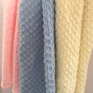 May include: Three crocheted baby blankets in pink, light blue, and cream colors. The blankets are made with a textured stitch and have a scalloped edge.