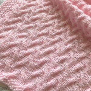 May include: A pink knitted baby blanket with a woven cable pattern.