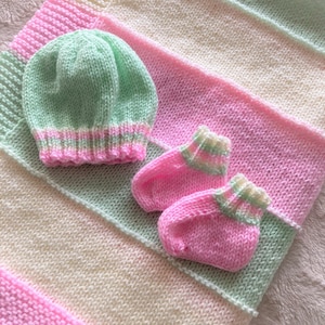 May include: A knitted baby blanket in pink, green, and white stripes with a matching knitted hat and booties.
