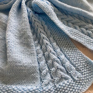 May include: A light blue knitted baby blanket with a cable knit pattern.