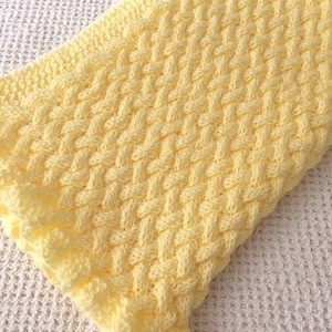 May include: A yellow knitted baby blanket with a woven pattern. The blanket has a delicate crocheted border.