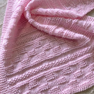 May include: A pink knitted baby blanket with a textured pattern.
