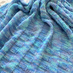 May include: A blue and green knitted blanket with a textured pattern. The blanket is made of soft yarn and has a cozy feel.