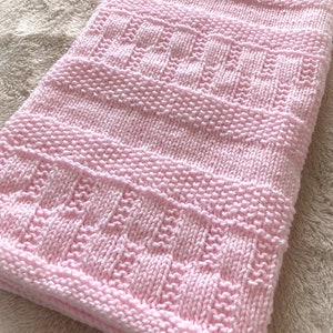 May include: A pink knitted baby blanket with a textured pattern.