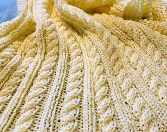 May include: A soft, yellow knitted baby blanket with a cable knit pattern.