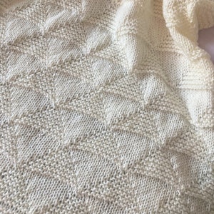 May include: A white knitted blanket with a geometric pattern. The blanket is made of soft yarn and has a delicate texture.