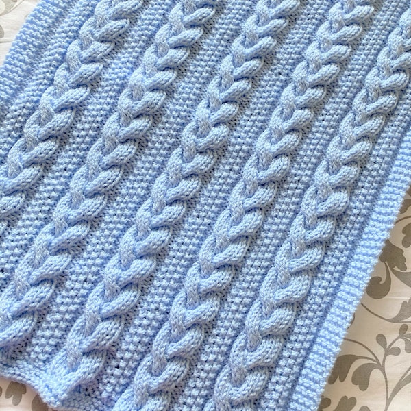 May include: A light blue knitted baby blanket with a cable knit pattern.