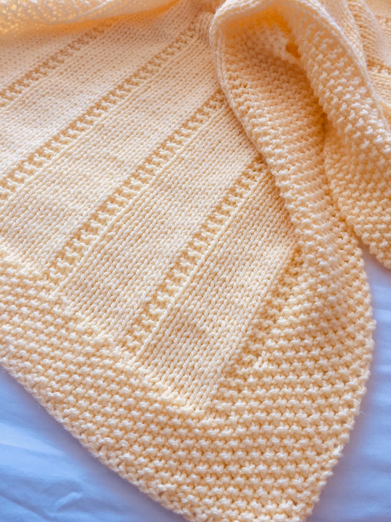 May include: A pale yellow knitted blanket featuring a combination of textured garter stitch borders and vertical panels of stockinette stitch separated by narrow rows of purl stitches, creating a soft and uniform appearance throughout the fabric.
