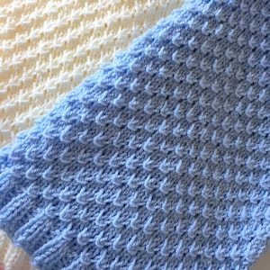 May include: Two knitted baby blankets, one in light blue and one in cream. The blankets are made with a textured stitch.