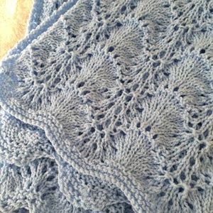 May include: A light blue knitted baby blanket with a delicate lace pattern.