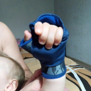 Könnte beinhalten: Ein dunkelblauer Stoff-Handhandschuh mit Daumenöffnung und einem grau gemusterten Band am Handgelenk. Der Handschuh verfügt über einen einfarbigen dunkelblauen oberen Teil und ein kontrastierendes blaues Innenfutter, das die Hand bedeckt.