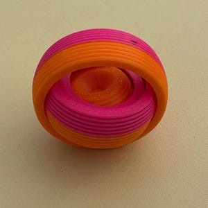 May include: A spherical fidget toy constructed from concentric, interlocking rings in alternating bright pink and vibrant orange colours. The object features a distinct 3D-printed texture with visible horizontal layers throughout its rounded, rotating structure.