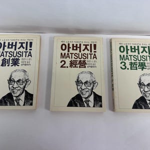 May include: Three softcover books titled Matsusita 1, 2, and 3, featuring a portrait of a man in glasses on each cover. The first book has blue text, the second has brown text, and the third has green text, all printed on a cream-colored background.