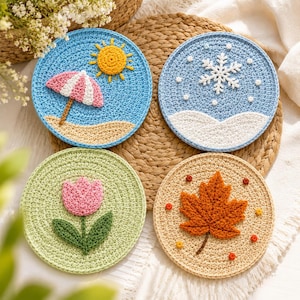 May include: Four circular crochet coasters representing the seasons. One features a yellow sun and pink beach umbrella on blue sand. Another shows a white snowflake on a blue background. A third displays a pink tulip on green. The last has an orange maple leaf.