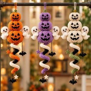 Könnte beinhalten: Drei hängende Häkeldekorationen mit gestapelten Kürbissen mit Jack-o'-Lantern-Gesichtern, flankiert von kleinen weißen Geistern. Unter jedem Kürbisstapel befindet sich ein spiralförmiger Schwanz in Orange, Lila oder Grün, verziert mit kleinen Sternen und schwarzen Fledermäusen.