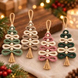 Könnte beinhalten: Vier handgefertigte Makramee-Weihnachtsbaumanhänger aus geschlungenen Kordeln in Salbeigrün, Beige, Altrosa und Dunkelwaldgrün. Jeder Baum ist mit weißen Kunstperlen, einer Jute-Aufhängeschlaufe oben und einer beigen Quaste am unteren Ende verziert.