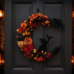 Puede incluir: Una corona en forma de media luna con una mezcla de flores artificiales y rosas negras, naranjas, rojas y amarillas. Una silueta negra de una bruja sosteniendo un murciélago se sitúa en la curva de la corona sobre una puerta oscura.