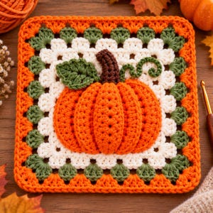 Puede incluir: Un cuadrado de ganchillo que presenta una calabaza naranja tridimensional en el centro con un tallo marrón y una hoja verde. La calabaza está rodeada por capas de puntos de hilo blanco y verde, rematada con un borde de color naranja.