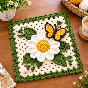 May include: A square crochet doily featuring a white daisy with a yellow center, green leaves, and small white buds. A yellow and brown butterfly is attached to the top right. The doily has a white center with a green scalloped border.