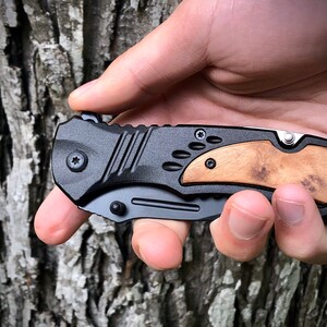 May include: A black folding knife with a wood handle. The knife has a textured black handle and a silver blade.