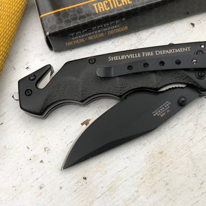 May include: Black folding knife with a safety blade and a pocket clip. The knife has the words "Shelbyville Fire Department" engraved on the handle.