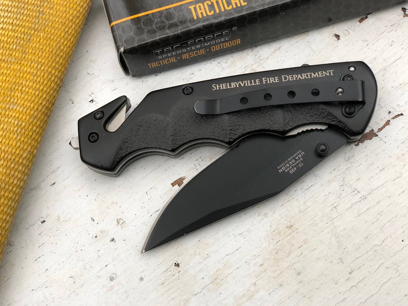 May include: Black folding knife with a safety blade and a pocket clip. The knife has the words "Shelbyville Fire Department" engraved on the handle.
