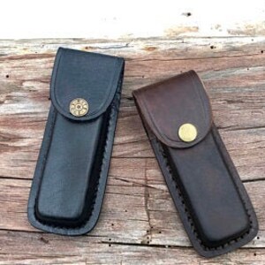 May include: Two leather knife sheaths, one black and one brown, with a brass button closure.