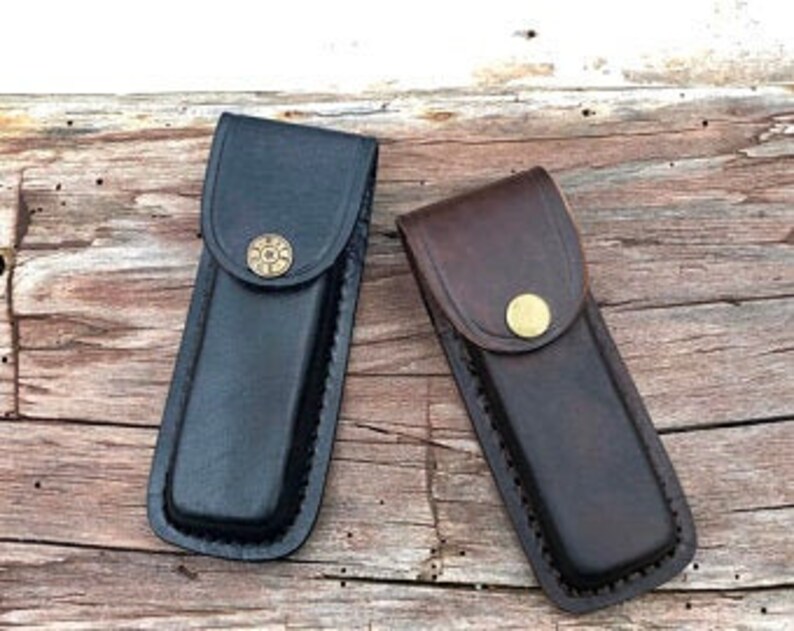 May include: Two leather knife sheaths, one black and one brown, with a brass button closure.