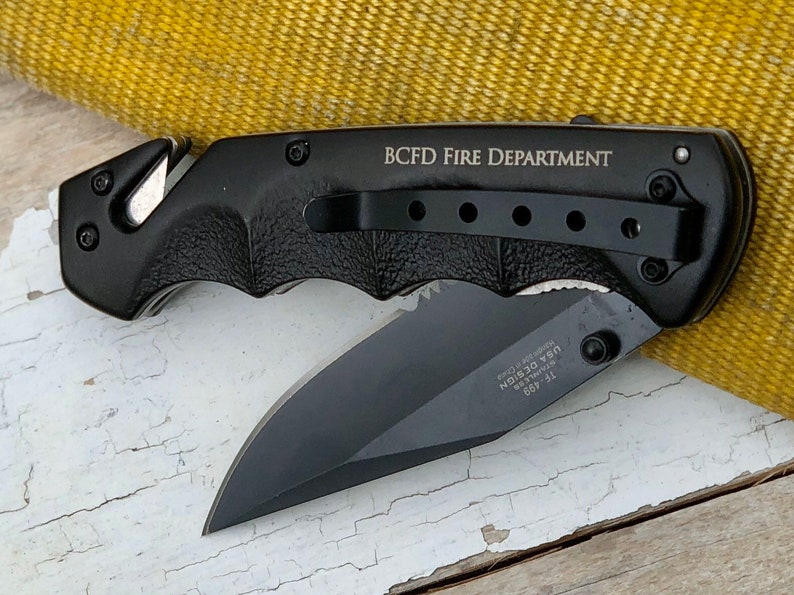 May include: Black folding knife with a black handle and a partially open blade. The handle has a pocket clip and the text "BCFD FIRE DEPARTMENT" is engraved on the side.
