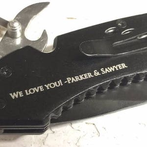 May include: Black multi-tool knife with a bottle opener, a blade, and a belt clip. The knife has an engraved message that reads "We love you! - Parker & Sawyer".