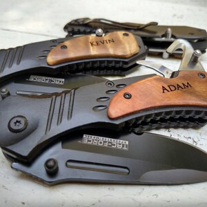 May include: Two black pocket knives with wooden handles. The handles are engraved with the names "Kevin" and "Adam".