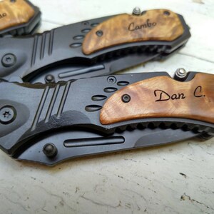 May include: Three personalized pocket knives with wood handles. The handles are engraved with the names "Fredo", "Cambo", and "Dan C."