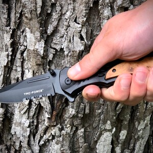 May include: A black folding knife with a serrated blade and a wood handle. The knife has the words "TAC-FORCE" printed on the blade.