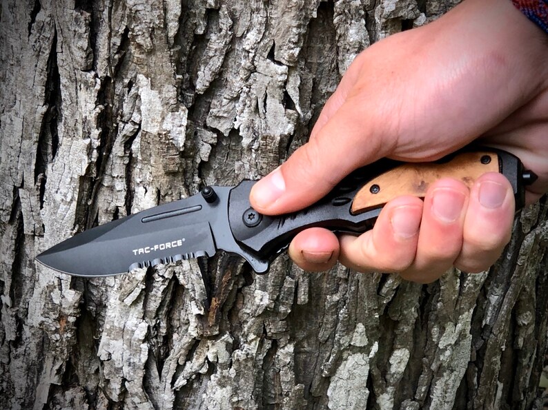 May include: A black folding knife with a serrated blade and a wood handle. The knife has the words "TAC-FORCE" printed on the blade.