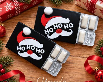 Puede incluir: Dos paquetes de chicles rectangulares negros con un gráfico de gorro y bigote de Papá Noel en rojo y blanco con el texto HO HO HO. Cada paquete incluye un pompón blanco y un blíster plateado que contiene cuatro piezas de chicle blanco.