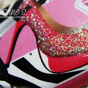 May include: Close-up of a pink and red high heel shoe with glitter on the toe. The shoe is on a white background with black and white stripes.