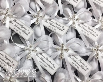 May include: White satin bows with silver cross charms and personalized tags that read "Lennon Angelina & Gino Valentino's Baptism, May 20, 2018".