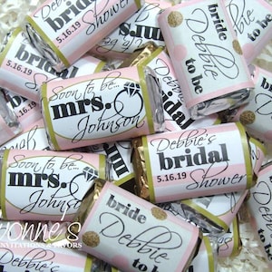 May include: Pink and white favor boxes with gold glitter accents. The boxes are decorated with the text "bride Debbie to be" and "Soon to be... mrs. Johnson".