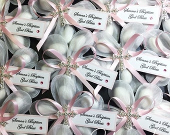 May include: Pink and white favor bags with a white satin ribbon and a silver cross with rhinestones. Each bag has a white card with the text "Sienna's Baptism God Bless".