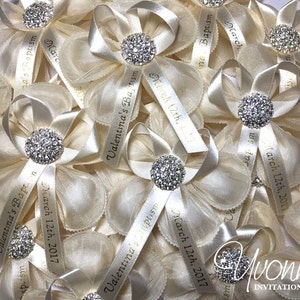 K&ouml;nnte beinhalten: Nahaufnahme von mehreren elfenbeinfarbenen Satinb&auml;ndern mit Strassstein in der Mitte. Jedes Band hat ein personalisiertes Band mit dem Text "Valentina's Baptism" und dem Datum "12. M&auml;rz 2017".