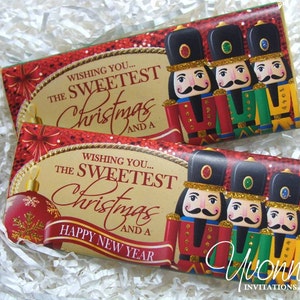 May include: Two chocolate bar wrappers with a Christmas theme. The wrappers feature a red and gold background with a nutcracker design. The text on the wrappers reads "Wishing you... the sweetest Christmas and a Happy New Year".