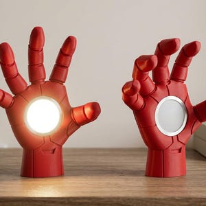 Può includere: Due sculture di mani robotiche rosse in posizione verticale. La mano sinistra presenta una luce bianca circolare illuminata nel palmo. La mano destra presenta una griglia per altoparlante circolare con bordo argentato nel palmo. Dita articolate.