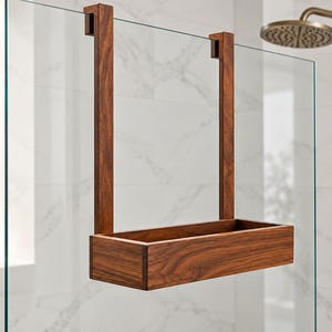May include: A rectangular dark brown wooden shower caddy with a visible wood grain pattern. The caddy features two vertical support arms that hook over the top edge of a glass shower panel, suspending the open-top storage bin in place.